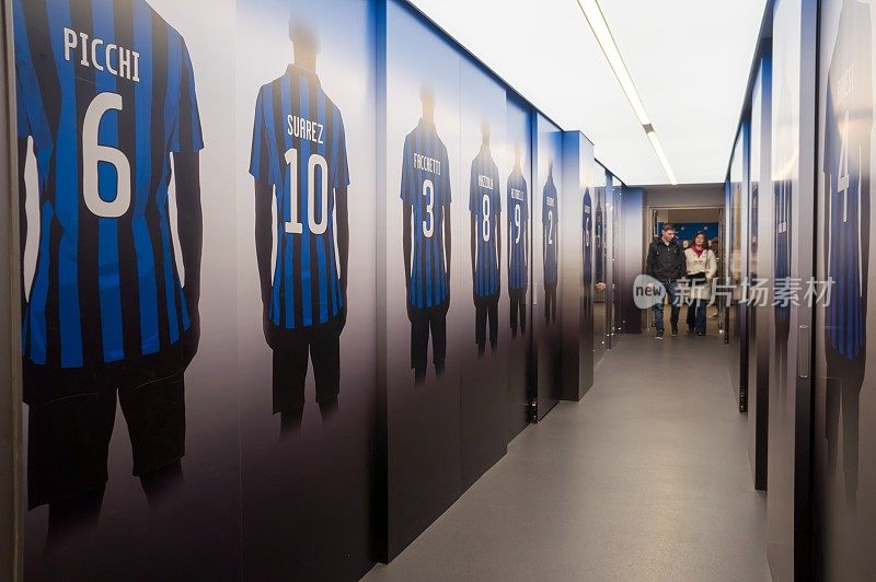1925年建成的圣西罗体育场(Giuseppe Meazza或圣西罗体育场)的墙上挂着足球运动员的画像，人们沿着走廊走着。